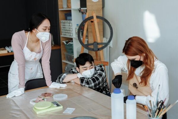 A diverse group engaging in a creative workshop, wearing protective masks and gloves for safety.