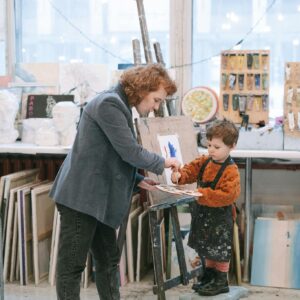 Adult assisting child with painting in a creative art studio setting.