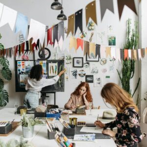 Artists paint in a bright, creative studio adorned with artwork and plants, fostering a vibrant atmosphere.
