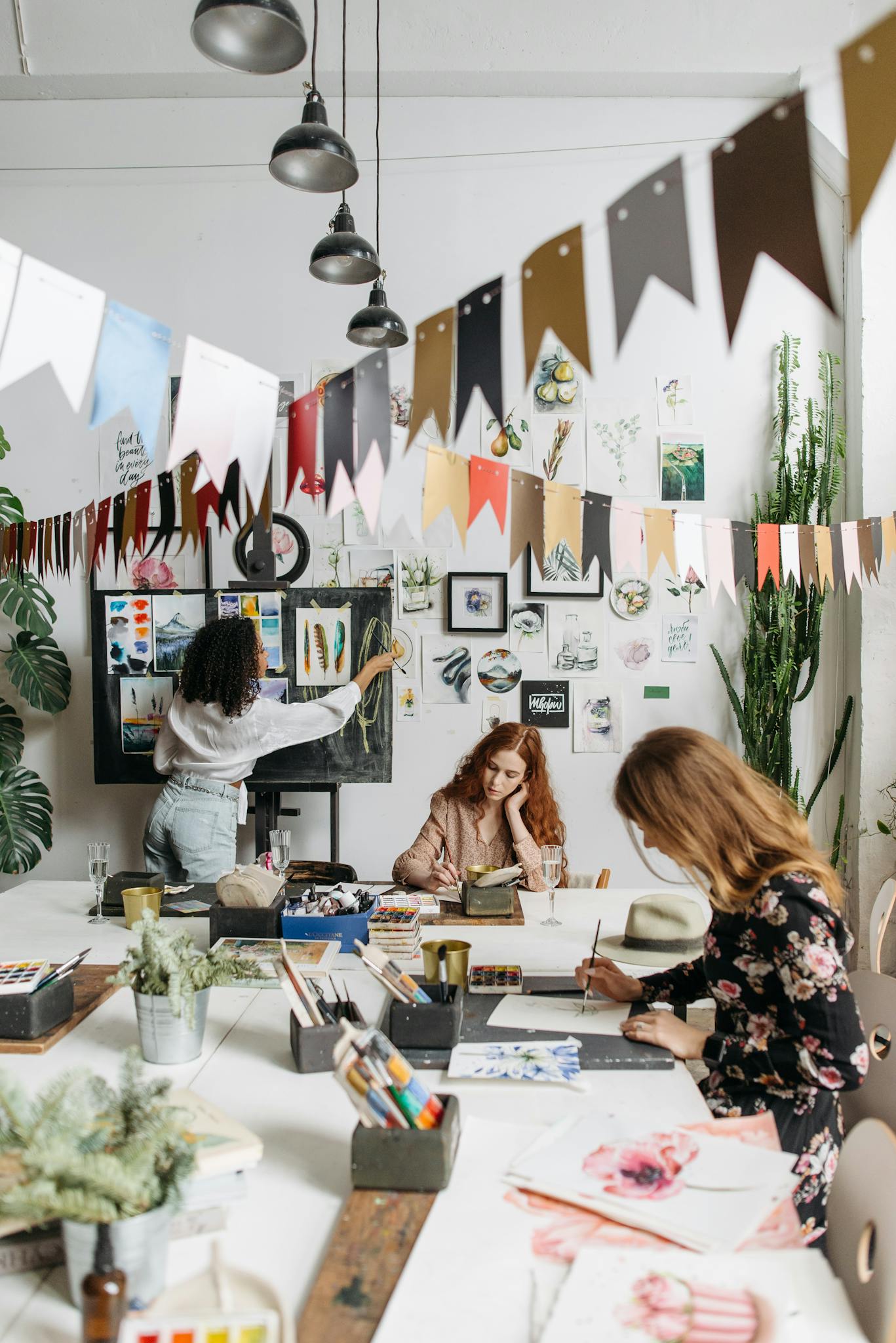 Artists paint in a bright, creative studio adorned with artwork and plants, fostering a vibrant atmosphere.