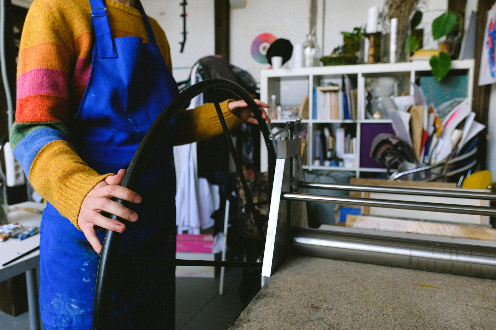 Side view of an artist operating a printing press in a colorful, creative studio.