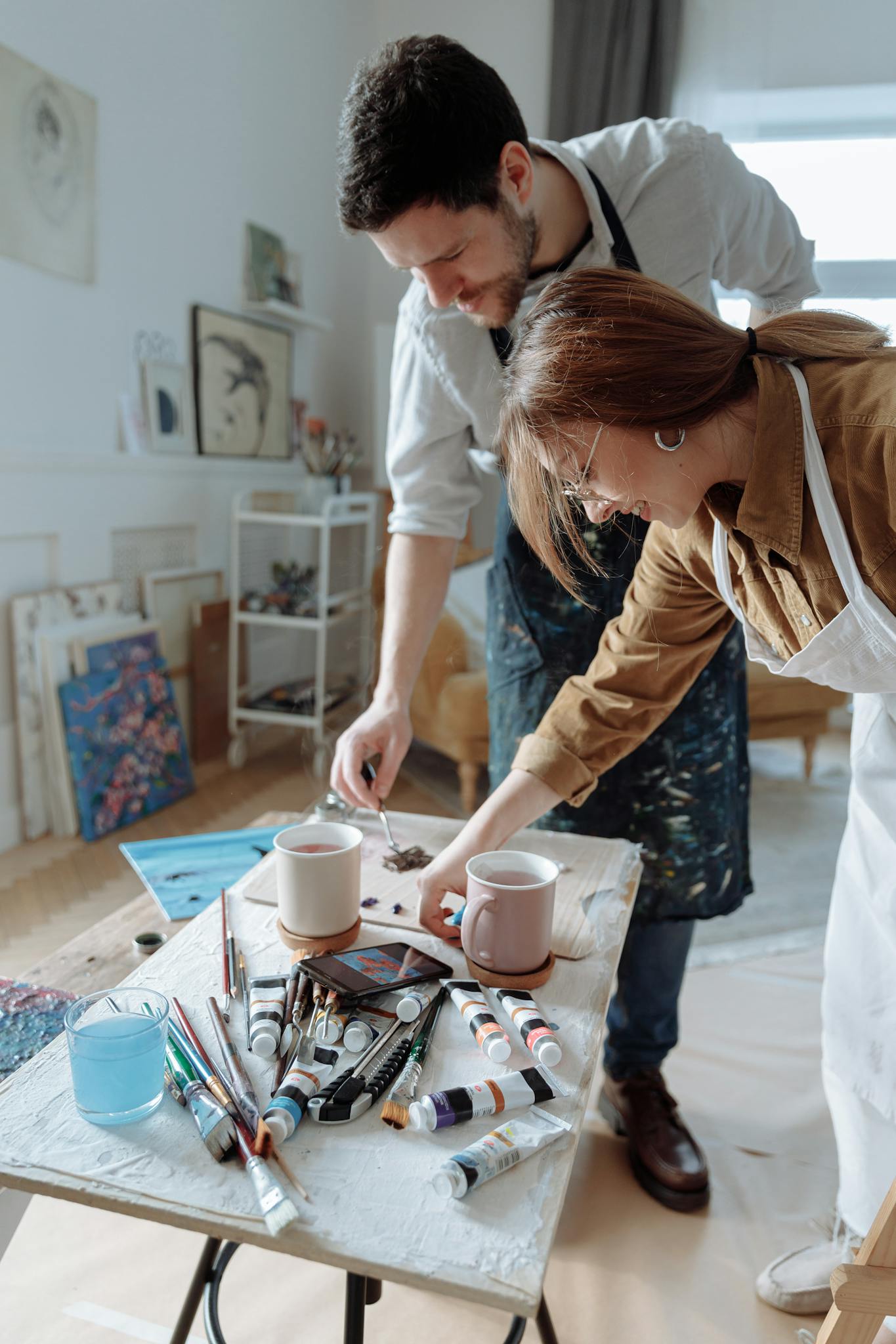 Two artists collaborating in a bright studio filled with art supplies.
